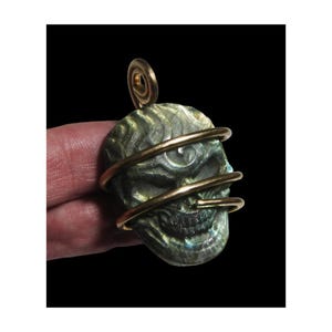 May include: A green and blue labradorite skull pendant wrapped in gold wire.