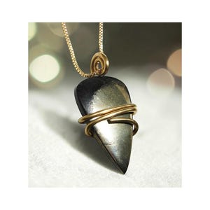 May include: A pendant necklace featuring a dark, teardrop-shaped stone wrapped in gold-colored wire. The stone hangs from a delicate gold chain, with a spiral detail at the top. The background is softly blurred.