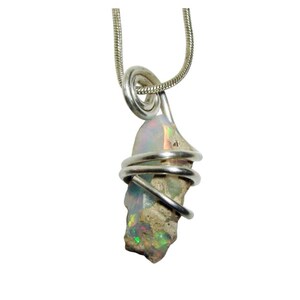 May include: A silver pendant necklace featuring a raw opal gemstone. The opal is wrapped in silver wire and suspended from a silver chain. The opal displays iridescent colors of green, orange, and blue.