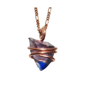 May include: A pendant necklace featuring a raw, faceted amethyst crystal wrapped in copper wire. The amethyst displays shades of purple and blue. The necklace has a gold-colored chain.
