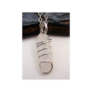 May include: A silver wire-wrapped clear quartz crystal pendant on a silver chain. The crystal is long, thin, and slightly cloudy.