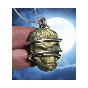 May include: A green stone skull pendant with a silver wire cage. The pendant is hanging from a silver chain.