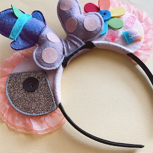 May include: Purple butterfly-shaped headband with pink tulle, a blue hat, a rainbow flower, a star, and a pink sweet. The headband is black.