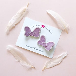 May include: Two purple felt bows with a glittery finish. The bows are on a white card with the text "giddy up and grow" and a small pink heart.