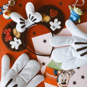 May include: A black and white headband with a Mickey Mouse design, two white gloves with black accents, and two Disneyland tickets. The headband has a black bow with white polka dots and a black and white Mickey Mouse head.