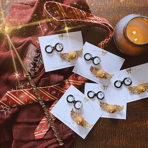May include: Six gold glitter and lightning bolt charm earrings with the text "giddy up and grow" on each card. The charms are on a red and gold striped background.