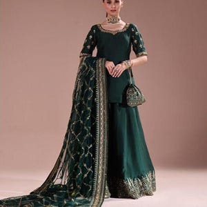 May include: A dark green formal outfit featuring a short-sleeved top, wide-leg pants, and a matching sheer scarf. The outfit is adorned with gold embroidery and embellishments. A small purse complements the ensemble.