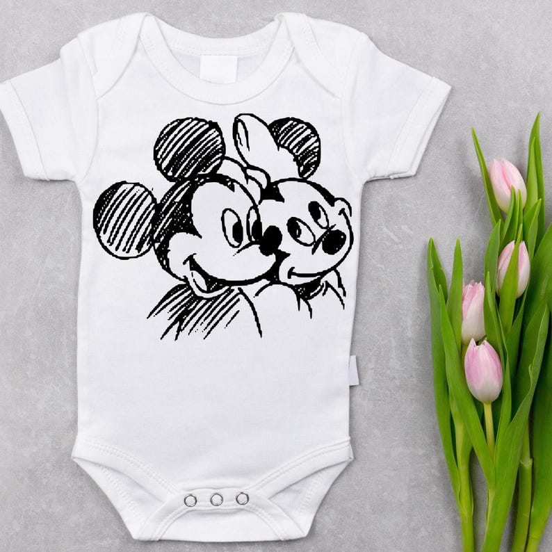 Pode incluir: Body de beb&eacute; branco com um esbo&ccedil;o a preto e branco do Mickey Mouse e da Minnie Mouse. O body de manga curta tem um fecho de encaixe. Tulipas cor-de-rosa com caules verdes no fundo.