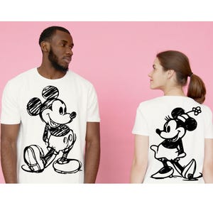 Pode incluir: T-shirts brancas com esbo&ccedil;os pretos de Mickey e Minnie Mouse. Uma t-shirt mostra Mickey na frente, a outra Minnie nas costas. Ambas t&ecirc;m gola redonda e mangas curtas, perfeitas para uso casual.