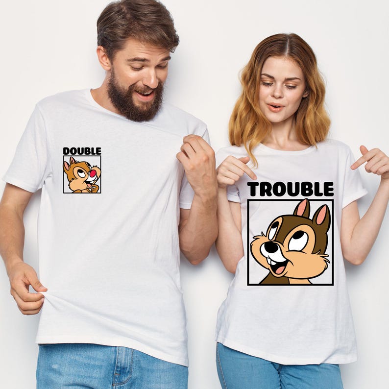 May include: Two white t-shirts with cartoon chipmunk graphics. One shirt says "DOUBLE" with a chipmunk image, the other says "TROUBLE" with a matching chipmunk. The shirts are worn by two people.