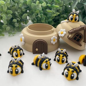 May include: A set of eight small, yellow and black bee figurines with brown eyes. The bees are arranged around a brown and white ceramic beehive with a small door and white flowers.