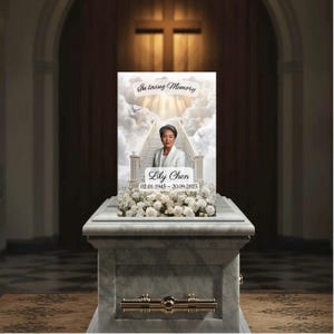 May include: A memorial portrait of Lily Chen, displayed on a white marble casket. The portrait features a woman in a white suit against a backdrop of clouds and stairs. Text reads "In loving Memory" and "Lily Chen 02.01.1945 - 20.09.2025". White roses adorn the casket.
