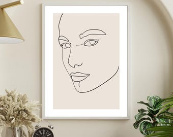 Könnte beinhalten: Ein gerahmter minimalistischer Kunstdruck mit einer schwarzen Strichzeichnung eines Gesichts auf beigem Hintergrund. Das Kunstwerk wird auf einem Holzregal mit einer goldenen Lampe, einem schwarzen Wecker und einer Vase mit Trockenblumen ausgestellt.