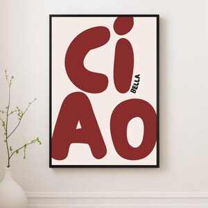 Könnte beinhalten: Ein gerahmter Kunstdruck mit dem Wort "CIAO" in großen, abgerundeten, kastanienbraunen Buchstaben auf cremefarbenem Hintergrund. Das Wort "BELLA" ist vertikal in Schwarz geschrieben. Der Rahmen ist schwarz.