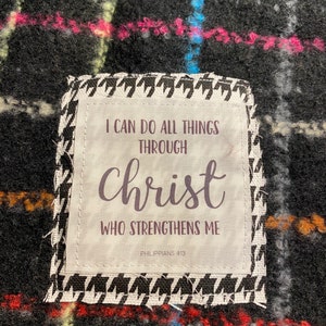 May include: A white fabric patch with black text that reads "I can do all things through Christ who strengthens me Philippians 4:13". The patch is sewn onto a black and white checkered fabric.