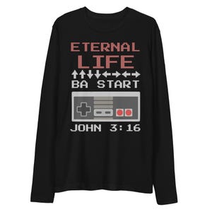 May include: Black long-sleeve shirt with a pixelated design. The design includes the words "ETERNAL LIFE" in red, a controller graphic, and the text "JOHN 3:16" in white. The shirt is made of a soft material.