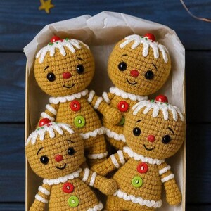 May include: Four handmade crochet gingerbread men dolls in a box. Each doll has a yellow body, white icing details, and a red cherry on top. They have black eyes, red noses, and green and red buttons.