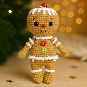 May include: A crocheted gingerbread man doll with a smiling face, black eyes, and a red nose. The doll is tan with white frosting details, red and green button accents, and a red cherry on top. A festive holiday decoration.