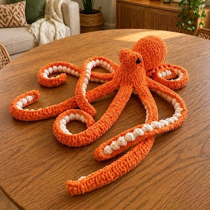 Könnte beinhalten: Eine handgefertigte gehäkelte Krake in leuchtendem Orange mit weißen Akzenten an den Tentakeln. Die Krake liegt auf einem Holztisch. Die Tentakel sind eingerollt. Die Krake hat schwarze Augen.