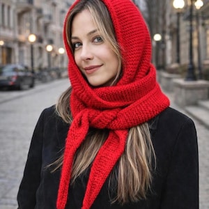 Może przedstawiać: Jasnoczerwony dzianinowy zestaw kaptur i szalik. Kaptur otacza twarz, a szalik układa się wokół szyi, z długimi wiązaniami. Zestaw wykonany jest z grubej, teksturowanej przędzy, idealny na zimną pogodę.