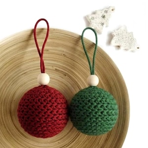 May include: Two crocheted Christmas ornaments. One is deep red with a matching cord and a wooden bead. The other is green with a green cord and a wooden bead. Two small white tree-shaped ornaments are in the background.
