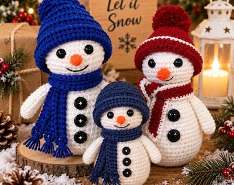 May include: Three crocheted snowmen figures with white bodies, black button eyes and torso buttons, and orange noses. One wears a blue hat and scarf, one a red hat and scarf, and the smallest wears a dark blue hat and scarf. They are arranged together.