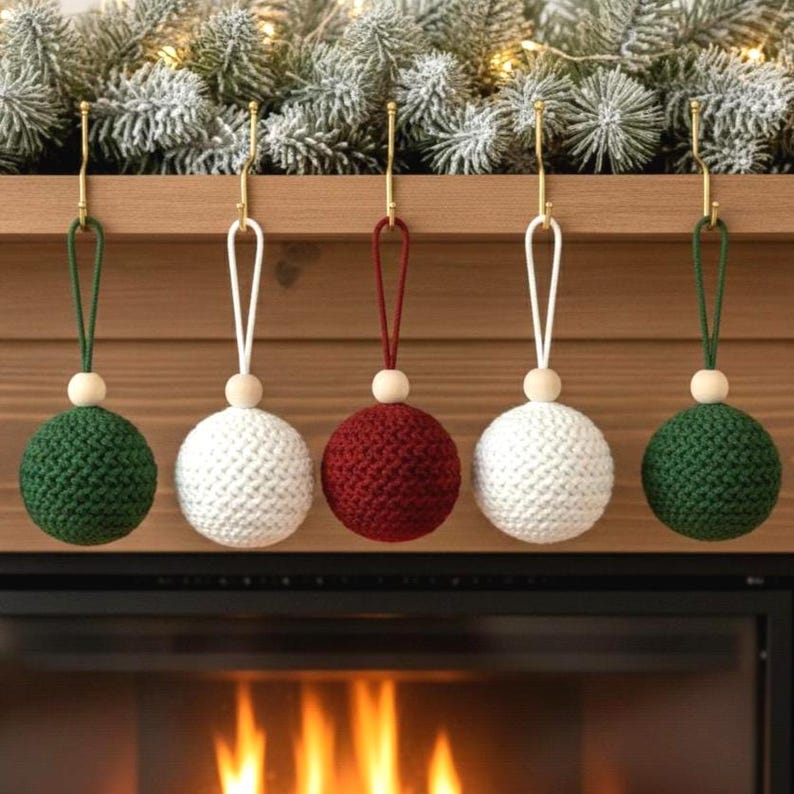 May include: Five handmade Christmas ornaments. Two are green, two are white, and one is red. Each ornament is a sphere made of knitted yarn, with a wooden bead and a hanging loop. The ornaments are hanging from gold hooks.