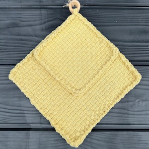 Può includere: Due presine da forno in crochet giallo con un anello di legno attaccato alla parte superiore.