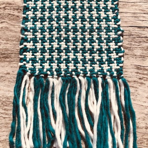 May include: A teal and white woven scarf with fringe on the ends. The scarf is made with a houndstooth pattern.