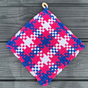 Puede incluir: Un agarrador de olla tejido en rosa, blanco y azul con un asa de bucle de madera.