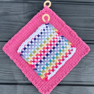 May include: A pink crocheted pot holder with a colourful woven square pot holder inside. Both pot holders have wooden rings for hanging.