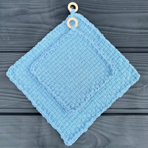 Può includere: Due presine da forno in crochet blu con anelli in legno per appenderle. Le presine da forno sono realizzate con un filato morbido e testurizzato.
