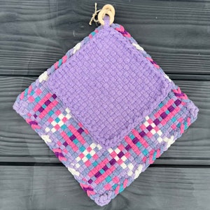May include: Purple and multi-colored woven pot holder with a smaller purple pot holder attached to it. The pot holders are made of yarn and have a woven design.