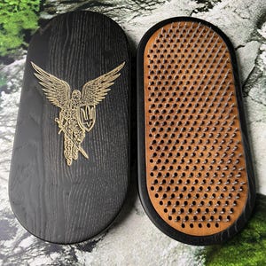 May include: Two oval wooden boards, one black with a gold-colored engraved winged figure holding a shield with a trident symbol, and the other featuring a light brown surface densely covered with rows of sharp, upright metal nails for standing.