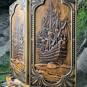 Könnte beinhalten: Ein Backgammon-Brett aus Holz mit einem geschnitzten Relief eines Segelschiffs. Das Brett ist braun mit goldenen Akzenten und einem dekorativen Rahmen. Backgammon-Steine in verschiedenen Farben sind vor dem Brett verstreut.