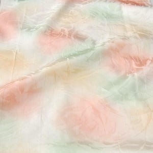 May include: A rectangular scarf featuring a soft, semi-sheer fabric with a delicate watercolor-inspired pattern. The design displays abstract, blended washes of pale peach, light green, and soft yellow hues across a white background.