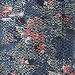 May include: Close-up of a textile with a dark blue background and a floral pattern. The pattern features red, white, and green flowers with blue and green leaves. The fabric has a woven texture.