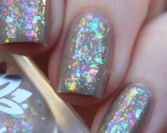 May include: Close-up of a light brown nail polish with iridescent glitter. The glitter is a mix of silver, gold, pink, blue, and green.