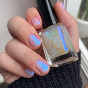 K&ouml;nnte beinhalten: Eine durchsichtige Glasflasche mit Nagellack, der einen leicht bl&auml;ulichen, irisierenden Schimmer hat. Die Flasche ist mit "Emily de Molly" beschriftet.