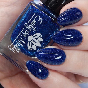 Pode incluir: Um frasco de vidro de verniz de unhas azul profundo com um acabamento de purpurina fina, apresentando o texto branco Emily de Molly e um log&oacute;tipo de flor de l&oacute;tus. O verniz &eacute; aplicado em unhas ovais, exibindo uma cor azul vibrante e brilhante.
