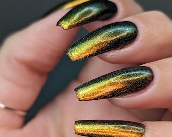 May include: Close-up of four long, almond-shaped nails painted with a dark green to gold iridescent nail polish. The nails are painted with a gradient effect, with the darkest green at the base of the nail and the gold at the tip. The nails are manicured and polished to a high shine. The text "@PolishedSteph" is visible on the image.