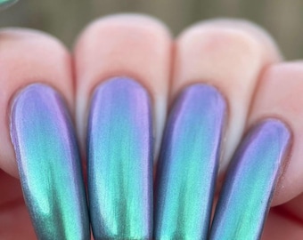 May include: Close-up of manicured nails with a color-shifting effect. The nails transition from a teal green at the base to a lavender purple at the tips. The polish has a glossy, iridescent finish.