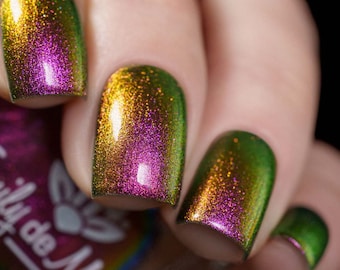 May include: Close-up of four fingernails painted with a green and gold iridescent nail polish. The polish shifts color in the light, showing shades of pink and green.