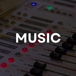May include: Close-up of a sound mixing console with the word "MUSIC" in white capital letters. The console has numerous sliders, buttons, and lights, with a dark background. The image suggests a recording studio or live performance setting.