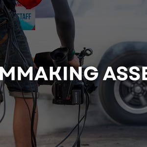 May include: A person holding a professional video camera, with the text "FILMMAKING ASSETS" in white. A white car is in the background, with smoke rising from the tires. The scene suggests a film production or automotive event.