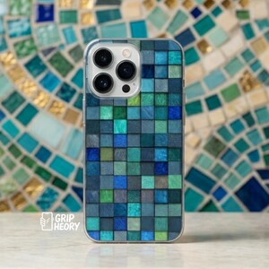 Può includere: Una custodia per smartphone con un motivo a griglia di piccole tessere quadrate in varie tonalità di blu, verde acqua e verde. Il design imita una superficie a mosaico con quadrati testurizzati. Il testo Grip Theory è visibile in basso a sinistra.