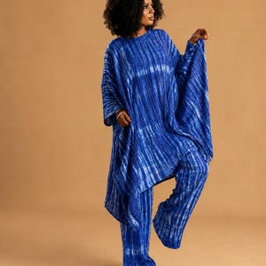 May include: A two-piece outfit consisting of a loose-fitting, long-sleeved tunic top and matching wide-leg trousers. The set features a vibrant blue and white tie-dye pattern with vertical stripes, creating a textured, flowing appearance.