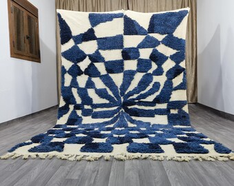 Può includere: Un grande tappeto geometrico con un sorprendente motivo blu e bianco. Il design presenta un motivo centrale a raggiera circondato da un motivo a scacchiera. Il tappeto ha un pelo spesso e un bordo sfrangiato. È appoggiato su un pavimento in legno.