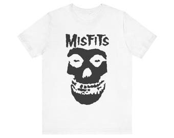 May include: White t-shirt featuring a black graphic of a skull with the word "MISFITS" above it in a bold, distressed font. The skull design has large eye sockets and a detailed jawline. The shirt is made of a soft material.