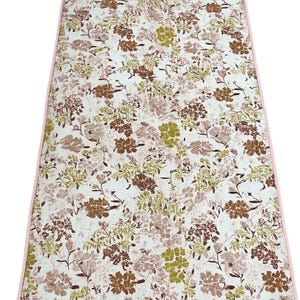 May include: Rectangular floral patterned mat with a pink border. The mat features a white background with a repeating pattern of brown, green, and pink flowers and foliage. The mat is likely made of fabric.